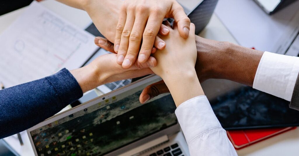 A diverse group of professionals stacking hands over a table symbolizing teamwork and collaboration.